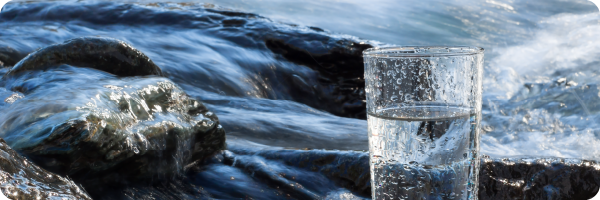 Stay hydrated when you're stopping drinking alcohol. Image shows a glass of water with a fast flowing river in the background. 