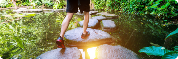 Cut back on alcohol a little each time you drink can help you stop drinking so much. Image hows a man walking across stepping stones on a calm river. 