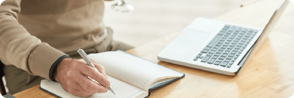 Making a plan can help you stop drinking. Image shows a man st at a desk in front of a laptop writing in a notebook. 