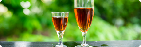 Make it a smaller one if you're stopping drinking. Image shows a smaller glass of rose wine next to a bigger glass with greenery in the background. 
