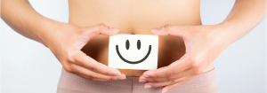 A person holding a drawing of a smiley face in front of their stomach to illustrate a happy gut.