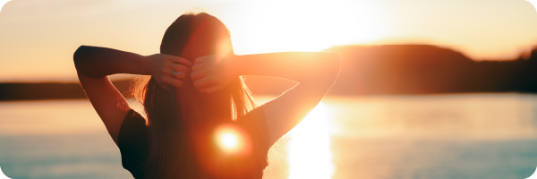 woman with her back to the camera looking out at the sun setting over water in a calming scene