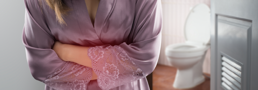 woman in dressing gown clutching her stomach denoting pain with a toilet in the background.