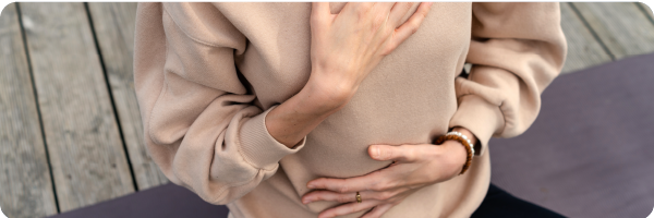 A woman's torso with one hand on her diaphragm and one hand one her stomach to illustrate how to be aware of your breathing and how to breathe well. 