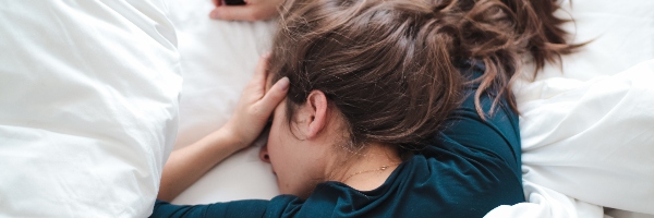 Woman in bed with her hands to her head, indicating a headache.