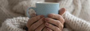 Person holding a warm mug at home indoors during cold weather.