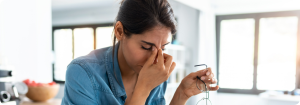 A stressed woman closes her eyes and pinches the bridge of her nose.