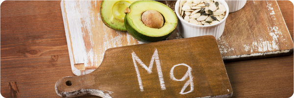 Check in on your magnesium intake sleep tip. Image shows 'Mg' written on a wooden board next to avocado and seeds which are high in magnesium.