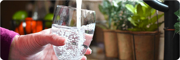 Keep hydrated sleep tip. Image shows a woman filling a glass of water up at the tap.