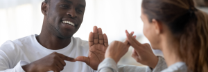 A young smiling black man and a young woman communicating with sign language.