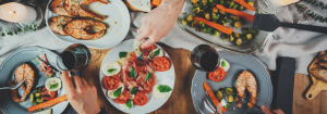 An bird's eye view of people eating food from a Mediterranean diet together, such as tomatoes, salmon, carrots and green vegetables.