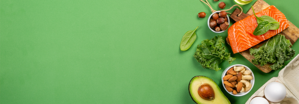 A photo of low carbohydrate foods like salmon, avocado, green leafy beg and nuts are shown on a green background.