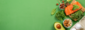 A photo of low carbohydrate foods like salmon, avocado, green leafy beg and nuts are shown on a green background.