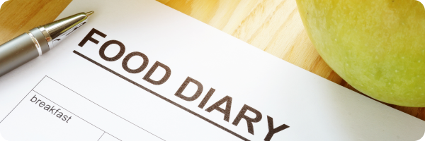 A photograph of a piece of paper with the title 'Food diary' on a desk, with a pen next to it and an apple.