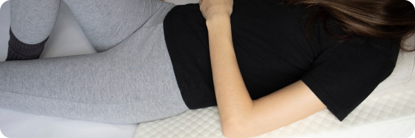 A person lying down in bed on a wedge pillow.