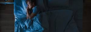 A man wearing a blue t-shirt lying on right asleep in bed.