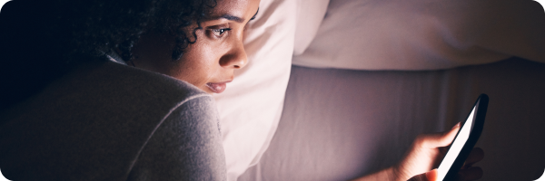 A woman lying on her side in bed. Her phone screen illuminates her face.