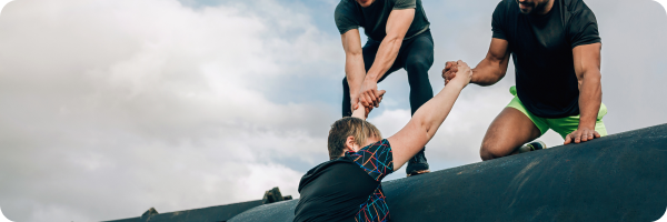 Two men helping pull another man up and over an obstacle course to represent that support networks should be used to help deal with nicotine cravings and withdrawal.