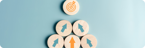 5 upwards pointing arrows on wooden circles, 4 are blue and one is orange. All the arrows point towards an orange icon of an arrow in the centre of a target in a bullseye position on a wooden circle. All on a blue background. 