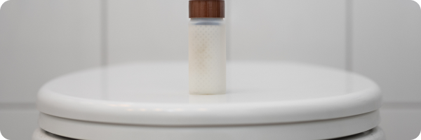 A sample jar on a closed toilet lid with the contents discretely hidden behind an white label. 