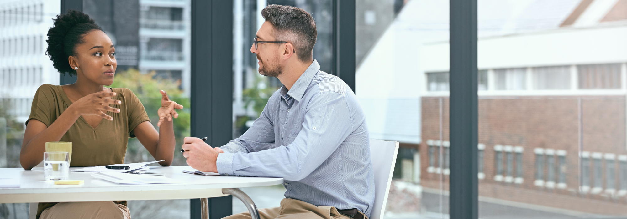 A professional looking woman and man sat at a table talking.