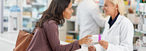 An young Asian woman holding some medication speaking to a smiling Caucasian pharmacist in a chemist.