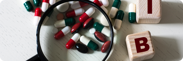 Pills under a magnifying class with the letters 'I' and 'B' on wooden square dice starting to spell out 'IBS'. 